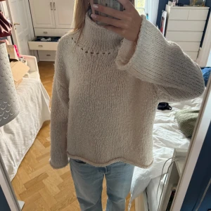Beige stickad polotröja från Zara - Mysig och chunky stickad polotröja från Zara i beige färg. Tröjan har en hög krage med dekorativa hål och långa ärmar med loose passform. Perfekt för kyliga dagar och enkel att styla med jeans eller kjol.