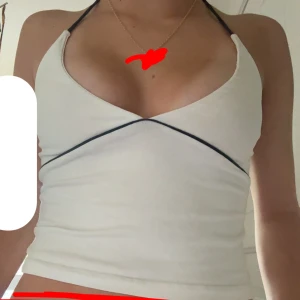 Vit halterneck topp från Subdued - Supersnygg vit halterneck topp från Subdued med mörkblåa detaljer och smala knytband i nacken. Toppen har en croppad passform och markerad söm under bysten som ger en cool look. Perfekt till jeans eller kjol för en trendig stil.