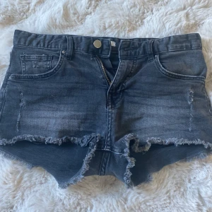 Mörkgrå jeansshorts med fransig kant - Snygga mörkgrå jeansshorts med mid midja och fransig, rå kant nertill. Klassisk femficksmodell med dragkedja och knapp framtill. Lätta att styla!
