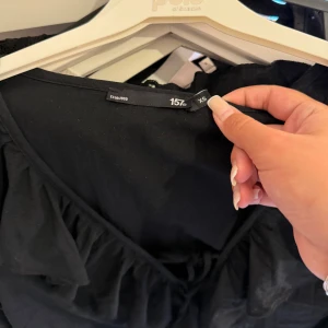 Svart omlottblus med volanger XS - Svart omlottblus från 157 i storlek XS. Blusen har en djup v-ringning med snygga volanger längs kanten och ett knyt framtill. Långärmad och tillverkad i mjukt bomullstyg som känns skönt mot huden. Perfekt för dig som gillar en feminin och trendig look. (Den är dammig pmed bilden men tvättas självklart innan ja postar) OANVÄND 