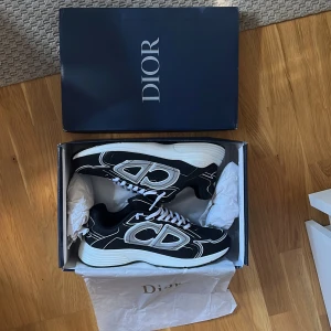 Dior b30 - Använt fåtal gånger och är i mycket bra kvalitet. Fick av min brorsa i födelsedagspresent när han var i Frankrike men vill ha pengarna!                  Snygga svarta Dior sneakers med vita och silverfärgade detaljer samt tydlig CD-logga på sidan. Skorna har vit och svart grov sula, mesh och syntetmaterial i ovandelen samt vita snören. Perfekta för dig som vill sticka ut med exklusiva och trendiga sneakers. 