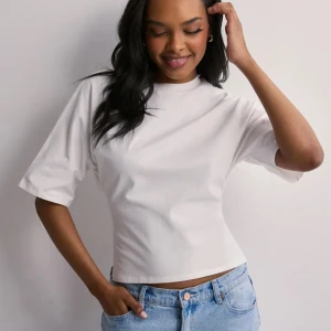 Vit croppad topp med knyt i ryggen/Open Back Tie Tee - Säljer en vit topp med korta ärmar och knytning i ryggen från Nelly. Perfekt att styla med t.ex. jeans. Säljer pga jag ej använder.