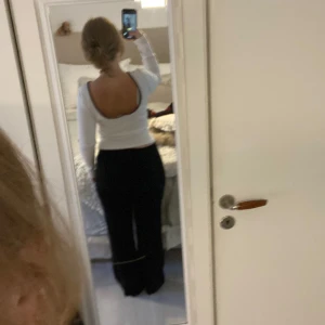 Vit ribbad topp med öppen rygg - Säljer en vit långärmad topp med svart kant runt den djupa, öppna ryggen och halsen. Ribbad och figurnära passform som sitter snyggt på kroppen. Kan bäras som en urringad topp eller som en topp som är öppen i ryggen.