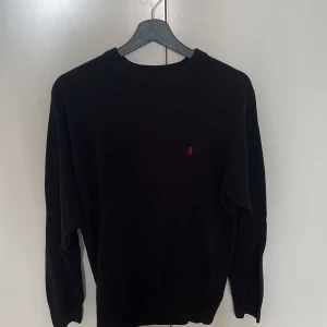 Svart kashmirtröja Polo Ralph Lauren - Svart tröja i 100% kashmir från Polo Ralph Lauren. Klassisk rund halsringning och diskret röd broderad logga på bröstet. Mjuk och lyxig känsla, perfekt för dig som gillar stilrena och exklusiva plagg. Långärmad och normal passform.