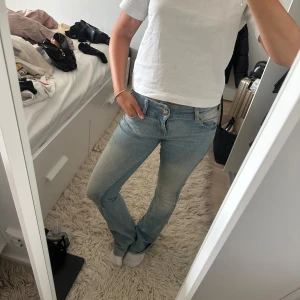 Ljusblå bootcut jeans - Säljer ett par ljusblå jeans med bootcut passform och klassisk femficksdesign. Jeansen har en låg midja och är tillverkade i mjukt denimtyg som sitter snyggt över höfterna och låren. Perfekta för dig som gillar en avslappnad men ändå trendig look.