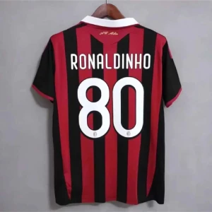 AC Milan Ronaldinho fotbollströja - Snygg AC Milan fotbollströja med Ronaldinho och nummer 80 på ryggen. Tröjan är röd och svart med vertikala ränder, vit krage och korta ärmar. Perfekt för dig som älskar klassiska fotbollströjor och vill hylla en legend.