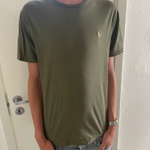  Olivgrön T-shirt från Polo Ralph Lauren - Tjenare säljer denna Snygg olivgrön t-shirt från Polo Ralph Lauren. Slim fit-modell med broderad logga på bröstet.  Perfekt för dig som gillar stilrena och enkla plagg. 10/10 skick inga definitioner. Ny pris: 1000kr mitt pris:500kr. Modellen är 181 cm och väger runt 60 kg. Tveka inte att höra av er! Mvh ville.