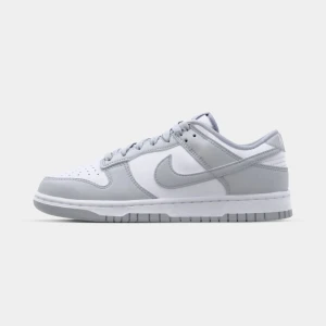 Nike Dunk Low vit/grå sneakers - Nike Dunk Low sneakers i fräsch vit och ljusgrå färg. Klassisk siluett med lågt skaft, perforerad tå och snörning. Ovandel i skinn och syntet, med ikonisk Swoosh på sidorna. Perfekta för dig som gillar clean och stilren streetwear.