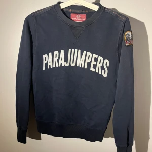 Mörkblå sweatshirt från Parajumpers - Snygg mörkblå sweatshirt från Parajumpers med stort vitt tryck på bröstet och patch på ärmen.   Tröjan har krympt väldigt mycket så bra köp om du har småsyskon som är 10-11 år 