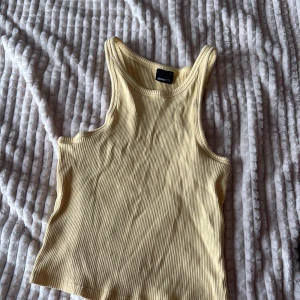 Ribbad gul linnetopp från Gina Tricot - Supersnygg ljusgul ribbad linnetopp från Gina Tricot i storlek S med sitter som XXS. Modellen är croppad med breda axelband och rundad halsringning. Perfekt för varma dagar och enkel att styla med jeans eller kjol. Materialet är mjukt och stretchigt för skön passform.