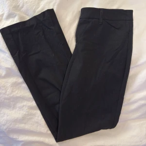 Svarta kostymbyxor  - Svarta kostymbyxor med klassisk rak passform. Byxorna har hällor för bälte, två bakfickor med knapp och är tillverkade i ett slätt tyg som ger en clean look. Perfekta för en stilren outfit.