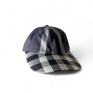 Rutig keps från Burberry i svart och blå - Snygg keps från Burberry med klassiskt rutigt mönster i svart, grått och vitt. Kepsen har böjd skärm och justerbar baksida. Materialet är mjuk bomull med en lyxig känsla och den ikoniska Burberry-loggan broderad baktill.