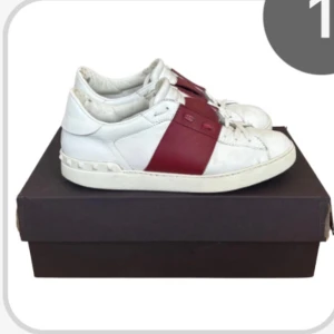 Valentino Open sneakers vit/röd skinn - Snygga Valentino Open sneakers i vitt skinn med bred röd rem över mitten. Klassisk låg modell med rund tå och platt sula. Ikoniska nitar längs hälen ger extra edge. Perfekta för dig som gillar exklusiva och trendiga sneakers. Köpta på store enda 100% äkta 6,5/10 skick, fråga gärna om fler bilder.     Kan gå ner i pris vid snabb affär. Storlek 42 två men sitter mer som 43