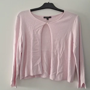 Ljusrosa kofta från Esprit - Säljer en söt ljusrosa kofta från Esprit med rund hals och en liten knapp framtill. Koftan har långärmade ärmar med en snygg v-formad detalj vid ärmslutet. 