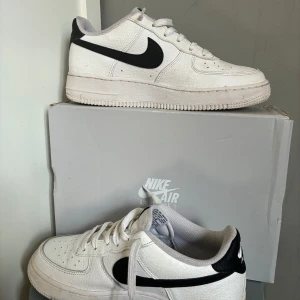 Nike Air Force 1 vita och svarta storlek  - Klassiska Nike Air Force 1 sneakers i vitt skinn med svart swoosh och svart detalj på hälen. Lågt skaft, rund tå och snörning framtill. Perforerade detaljer på tån för extra ventilation. Perfekt för dig som gillar en clean och tidlös look.