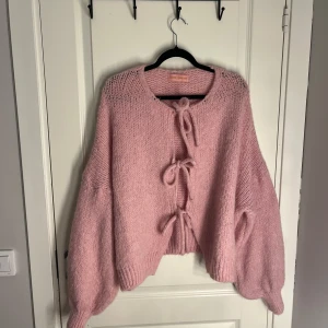 Rosa stickad kofta från Love Forever - Supermysig rosa stickad kofta från Love Forever med tre knytband framtill. Koftan har en loose passform och ballongärmar som ger en chill vibe. Materialmix med mohair, ull och syntet gör den fluffig och skön. Perfekt för lager-på-lager under hösten och vintern. Priset går att diskutera vid snabb affär 