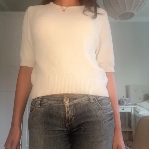 Vit stickad tröja med kort ärm - Säljer en vit stickad tröja med korta ärmar och rund hals. Tröjan har ribbade muddar vid ärmslut och nederkant, vilket ger en snygg och enkel look. Perfekt att matcha med jeans eller kjol för en clean stil. Zara har konstiga storlekar så det är M men sitter som en S