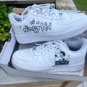 Nike Air Force 1 Wimpy Kid custom - Unika vita Nike Air Force 1 sneakers med handritade Wimpy Kid-motiv i svart på sidorna. Klassisk låg modell med snörning, perforerad tå och platt sula. Skorna är i skinn och har en clean look med coola detaljer som sticker ut. Köpt för ca 4700 , pris går att diskutera, bara att ställa frågor :) kan ta byten, 