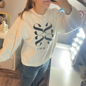 Vit sweatshirt från Gina Tricot - Säljer en vit sweatshirt från Gina Tricot i storlek L. Tröjan har ett stort svart tryck med coolt grafiskt motiv och rund hals. Materialet är mjukt och med ribbade muddar vid ärmslut och nederkant. Finns en fläck på insidan av tröjan i nedre kanten men det syns inte igenom bara skönt att veta!:)