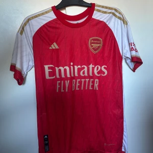 Arsenal hemmatröja Adidas röd/vit - Säljer en officiell Arsenal hemmatröja från Adidas med blixtmönster i rött och guldiga detaljer. Den är knappt använd och är i helt nytt skick. Den är i S och är köpt ifrån adidas!