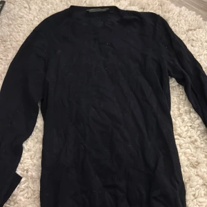 Marinblå  långärmad stickad tröja - Svart stickad tröja från Zara med långa ärmar och ribbade muddar. Snygga guldfärgade knappar vid ärmsluten ger en extra detalj. Perfekt för dig som gillar stilrena och klassiska plagg med en twist.