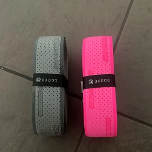 Oxdog grepplinda - Två snygga grepplindor från Oxdog, ett i grått och ett i starkt rosa. Båda har perforerat mönster med små prickar och Oxdog-loggan tryckt längs hela bältet. Perfekt för dig som vill sticka ut med sportig stil. Säljes tillsammans.