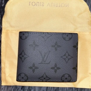 Svart Louis Vuitton plånbok i skinn - Snygg svart plånbok från Louis Vuitton med klassiskt monogrammönster. Plånboken är tillverkad i äkta skinn och har flera fack för kort och sedlar. Perfekt storlek för att ha med sig överallt.