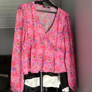 Blommig volangblus från BikBok - Superfin blommig blus från BikBok i rosa och lila toner. Blusen har v-ringning, långa ärmar och volangdetaljer framtill. Perfekt för dig som gillar färg och romantiska vibes. Luftigt material som känns lätt och skönt.🩷💜