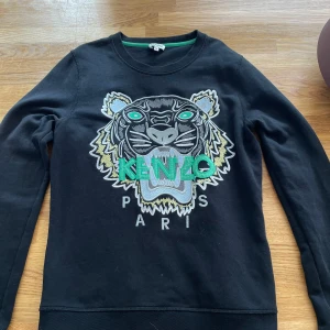 Svart Kenzo tröja  - Svart långärmad tröja från Kenzo med ikoniskt broderat tigerhuvud i grått, grönt och gult framtill. Stort Kenzo Paris-tryck över bröstet. Snygg och väldigt bra skick men används tyvärr inte längre💕 storlek M men tycker den sitter som S💕 skriv om frågor eller fler bilder