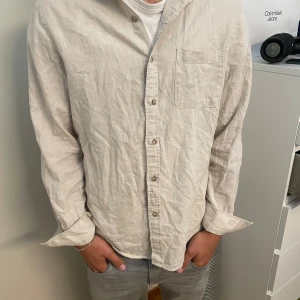 Beige linneskjorta från Dressmann M - Snygg beige skjorta från Dressmann i linnemix. Skjortan har klassisk krage, bröstficka och knäppning framtill. Långärmad och med avslappnad passform, perfekt till jeans eller chinos. Enkel och stilren design som funkar året runt.