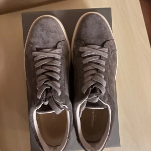 Grå mockasneakers från Vagabond - Snygga grå sneakers från Vagabond i mjuk mocka med vita, platta sulor. Skorna har klassisk rund tå, snörning och stilren design som passar till det mesta. Perfekta för dig som gillar en clean och modern look.