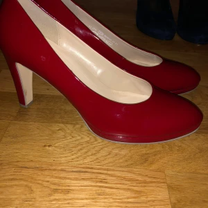 Röda pumps från Gabor med klack - Snygga röda pumps från Gabor med rund tå och hög klack. Skorna har en glansig finish och är tillverkade i syntetmaterial med ljus insida. Perfekt för dig som vill sticka ut med en djärv färg och klassisk form.