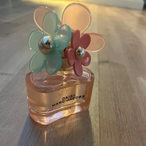 Daisy Daze parfym från Marc Jacobs - Säljer en Daisy Daze parfym från Marc Jacobs med en söt flaska i ljusrosa glas och dekorativt lock med stora plastblommor i mintgrönt och rosa. Flaskan har en modern, rundad form och blommorna har guldfärgade detaljer i mitten. Använd några gånger🩷