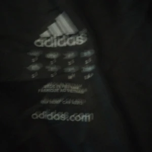 Svart Adidas vind jacka - Svart hoodie från Adidas med klassisk logga tryckt på insidan. Tröjan har huva och är tillverkad i mjuk bomull, perfekt för en chill och sportig look. Passar dig som gillar streetwear och vill ha något bekvämt och stilrent.