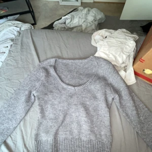 Grå ribbad stickad tröja med v-ringning - Säljer en snygg grå stickad tröja med ribbad struktur och v-ringad hals. Tröjan har långärmade ärmar och bred ribbad kant nedtill. Perfekt att matcha med jeans eller kjol för en chill look.