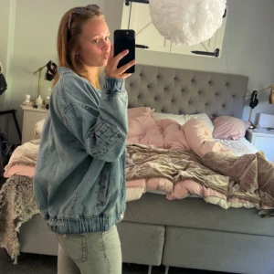 Oversized ljusblå jeansjacka - Säljer en oversized ljusblå jeansjacka med dragkedja och resår i midjan och vid ärmsluten. Jackan har en avslappnad passform och klassisk krage, perfekt att slänga över en hoodie eller crop top. Enkel och stilren design som funkar till det mesta.