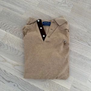 Beige långärmad pikétröja Ralph Lauren - Snygg beige långärmad pikétröja från Ralph Lauren med klassisk krage och knappar i halsen. Tröjan har en mörkbrun knappslå och den ikoniska broderade loggan på bröstet. Perfekt för dig som gillar stilrena och tidlösa plagg. Storlek S Nypris 1500