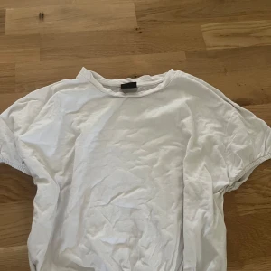 Vit t-shirt från Gina Tricot - En basic vit t-shirt från Gina Tricot i storlek XXS. T-shirten har rund halsringning och korta ärmar med lätt rynk vid ärmslutet. Tillverkad i mjuk bomull, perfekt för en clean och enkel look.