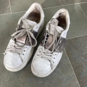 Valentino vita sneakers - Snygga vita sneakers från Valentino med bred metallic rem över sidan. Storlek 39. Finns defekter på dem.