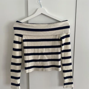 Randig offshoulder topp Stradivarius - Superfin ribbad offshoulder topp från Stradivarius i vitt och marinblått. Långärmad och croppad modell med bred, vikt kant upptill. Snyggt randigt mönster och stretchigt material! Använd 3 gånger.