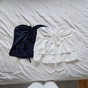 2 Volangtoppar  - Två stycken riktigt fina tubtoppar med volanger, blå och vit i storlek xs/s. Aldrig använda då de glömts bort i garderoben, perfekta till sommarn!