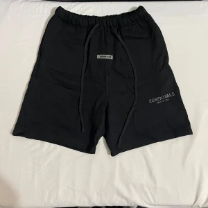 Svarta shorts från Essentials Fear of God - Svarta shorts från Essentials Fear of God med elastisk midja och snörning. Klassisk och enkel design med logga framtill. Perfekta för en avslappnad stil.