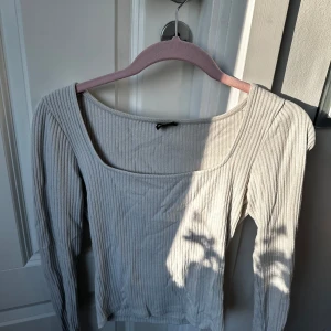 Ribbad beige topp från Gina Tricot - Säljer en ribbad, beige långärmad topp från Gina Tricot. Toppen har en fyrkantig urringning och sitter tight. Perfekt att styla med jeans eller kjol för en enkel och snygg look.