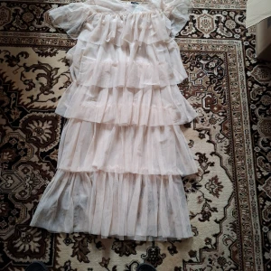 Ljus volangklänning med puffärm - Säljer en romantisk ljus klänning med flera lager volanger och puffiga korta ärmar. Klänningen har en luftig och flowy känsla, perfekt för sommarens alla tillfällen. Materialet är tunt och skirt, vilket ger en drömmig look.