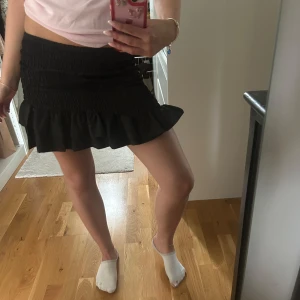 Svart volangkjol - Supersöt svart lågmidjad kjol med smock i midjan och volang nertill. Kjolen har en figurnära passform upptill och är perfekt att styla med en enkel topp. Bekväm och stretchig modell. 💗Helt ny, aldrig använd, nypris 399