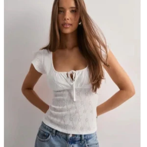 Vit broderad topp - Säljer denna söta sommartopp från Nelly, som är slutsåld på deras sida. Toppen är helt oanvänd då jag råkade dra av lappen när jag tänkte returnera den! Toppen är i storlek S