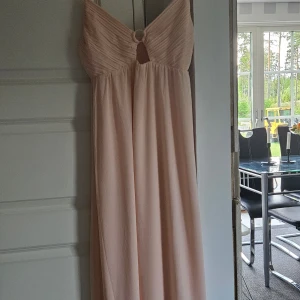 Ljusrosa långklänning med twistad överdel - Säljer en elegant ljusrosa långklänning med twistad överdel och liten öppning framtill. Klänningen har en mjuk, flytande passform och är ärmlös, perfekt för sommarens speciella tillfällen. Storlek M men passar även S . Stretchig:)