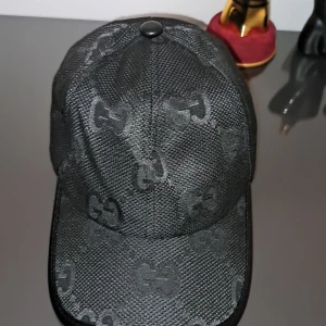 Svart keps från Gucci med GG-mönster - Snygg svart keps från Gucci med diskret GG-mönster över hela kepsen. Justerbar rem baktill för perfekt passform. Tillverkad i ett slitstarkt material med lätt glansig finish. Helt ny me kartongen på