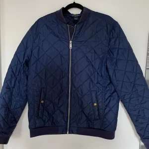 Blå bomberjacka från Polo Ralph Lauren - Säljer en mörkblå jacka från Polo Ralph Lauren. Jackan har dragkedja framtill, nederkant samt två fickor med tryckknapp. Klassisk och stilren design med hyfsat diskret logga på bröstet. Storleken på jackan står i barnstorlek så jackan är inte XL utan Xs/S (herrstorlek). 