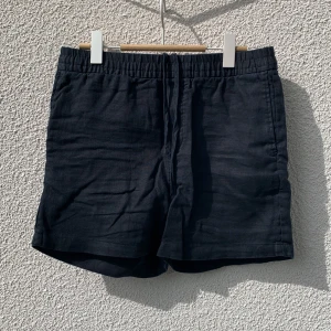 Svarta linneshorts från H&M - Svarta shorts i linne från H&M med elastisk midja och snörning. Klassisk rak passform med två bakfickor och diskret design. Storlek S.